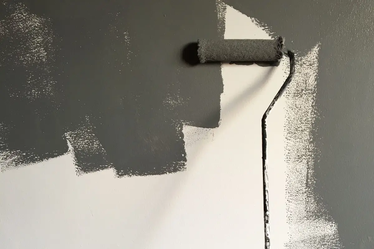 Paint roller applying gray paint over a white wall during a home renovation
